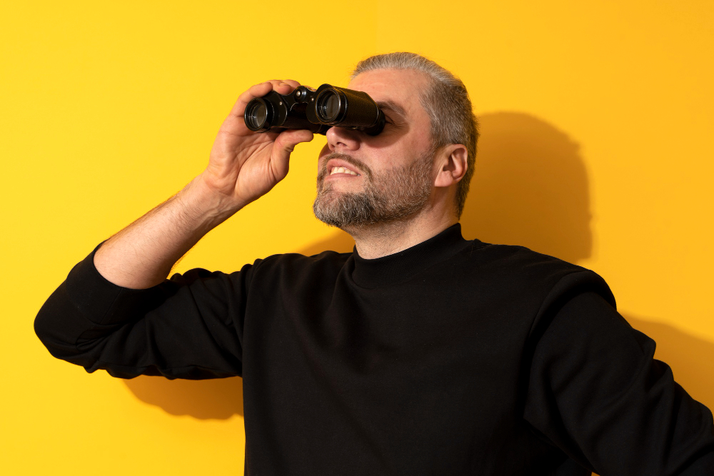 personne sur fond jaune qui regarde dans une direction donnée avec des jumelles.